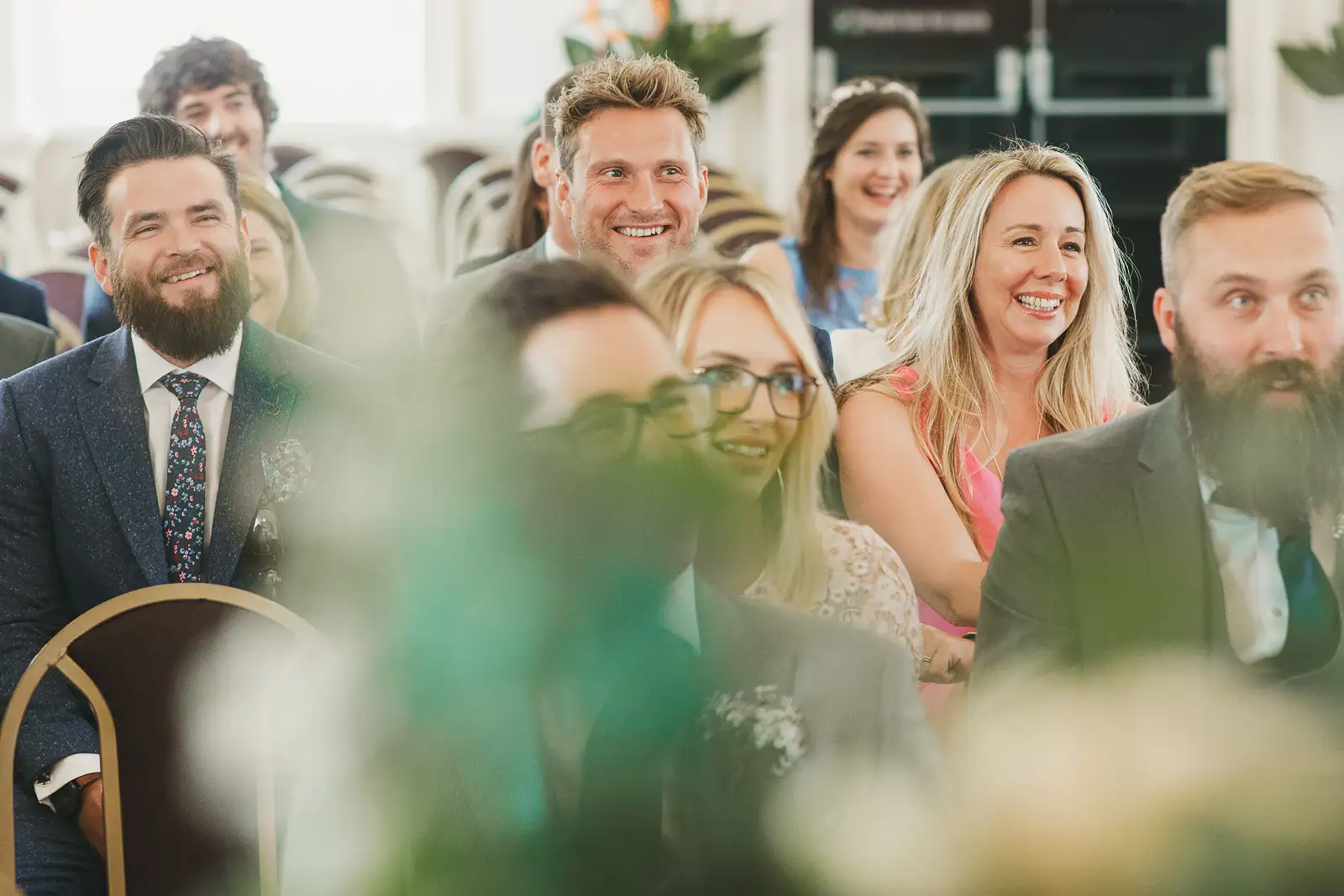 Wedding guests laughing and smiling during ceremony at Poole Guildhall Registry Office, shot through flowers