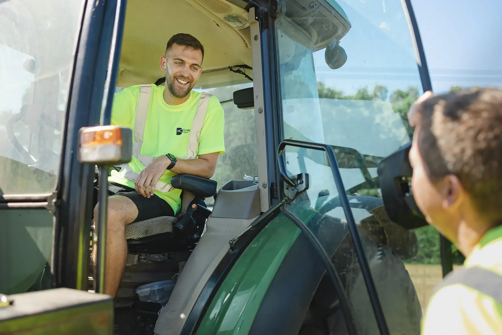 Young groundskeeper smiling in the cab of a tractor talking to a colleague at Moors Valley Country Park in Dorset