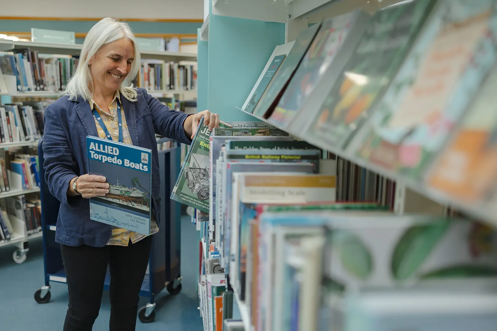 Smiling library worker browsing bookshelves and holding a book at Weymouth Library in Dorset