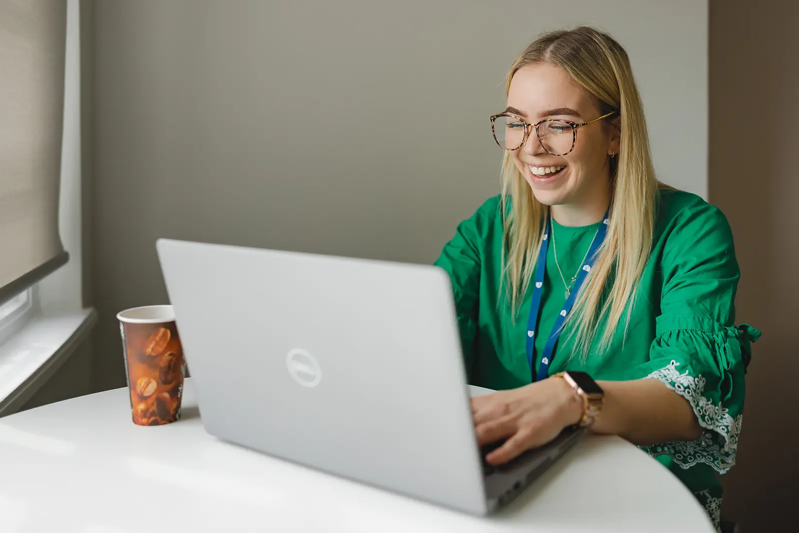 Young professional woman smiling at her laptop with a coffee cup beside her in a Dorset office, natural working portrait