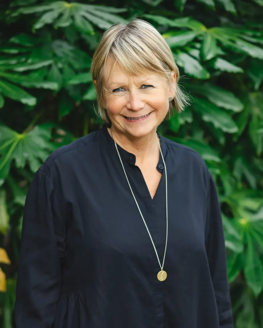Natural commercial portrait of a senior professional woman in navy against lush green foliage, warm and approachable, Dorset