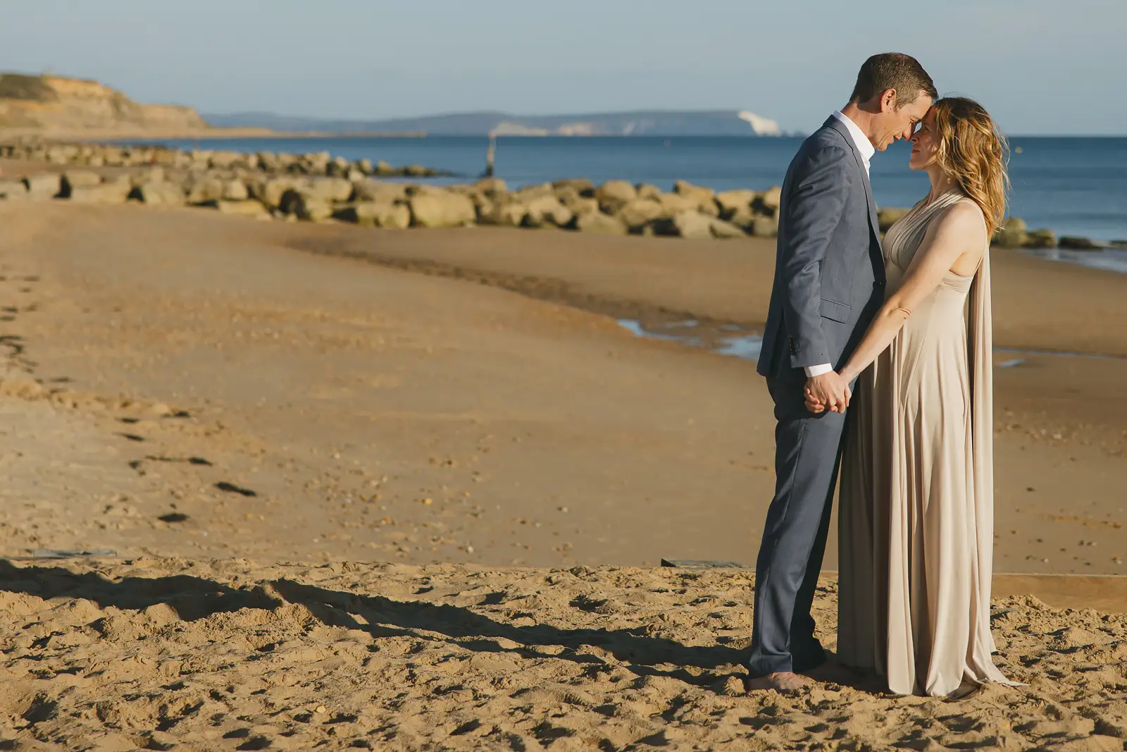Newlywed couple touching foreheads on sandy Bournemouth beach after Poole registry office wedding, rocky coastline behind