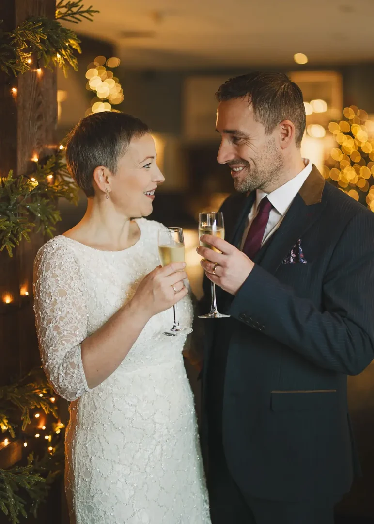 Bride and groom toasting with champagne glasses surrounded by warm Christmas lights after their Poole registry office wedding