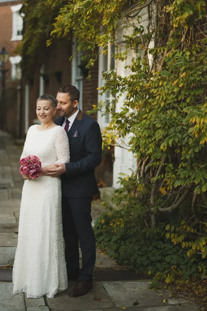 Newlyweds posing together against an ivy-covered wall on a historic Poole Old Town street after registry office wedding