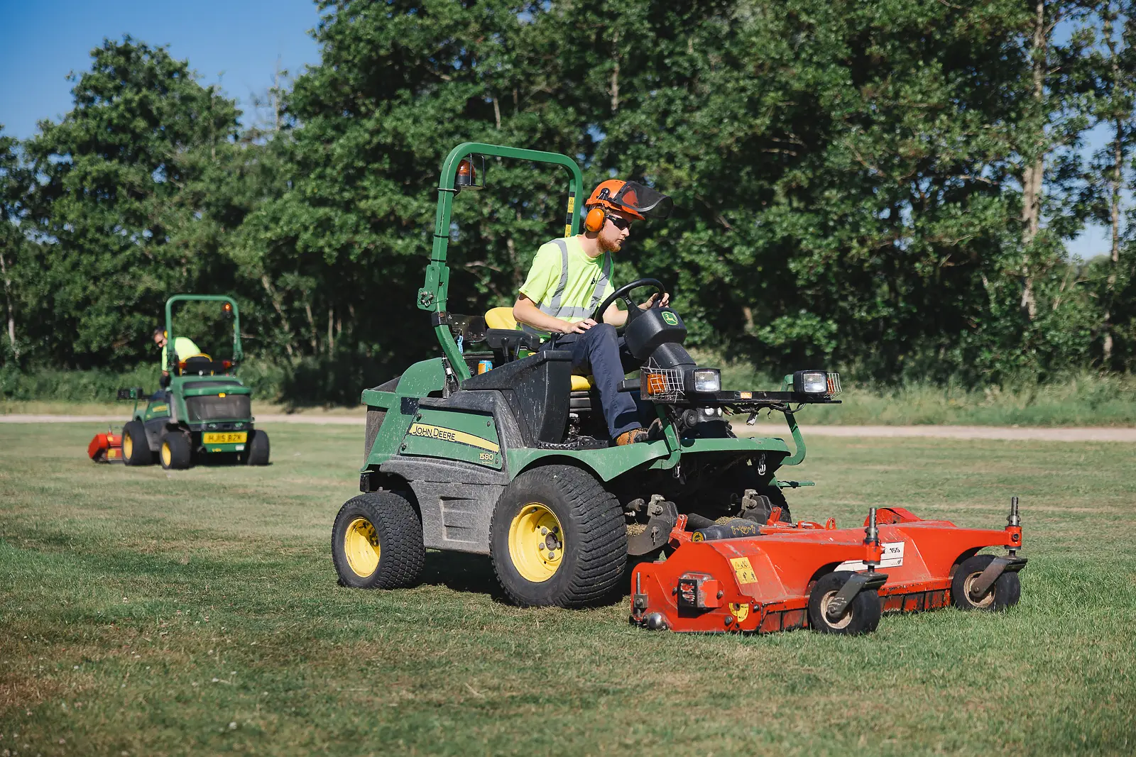 Grounds maintenance team operating John Deere ride-on mowers across open parkland at Moors Valley Country Park in Dorset