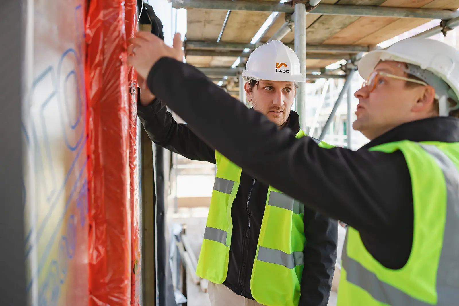 Two building inspectors in LABC hard hats and hi-vis closely examining construction details together at a Poundbury development site