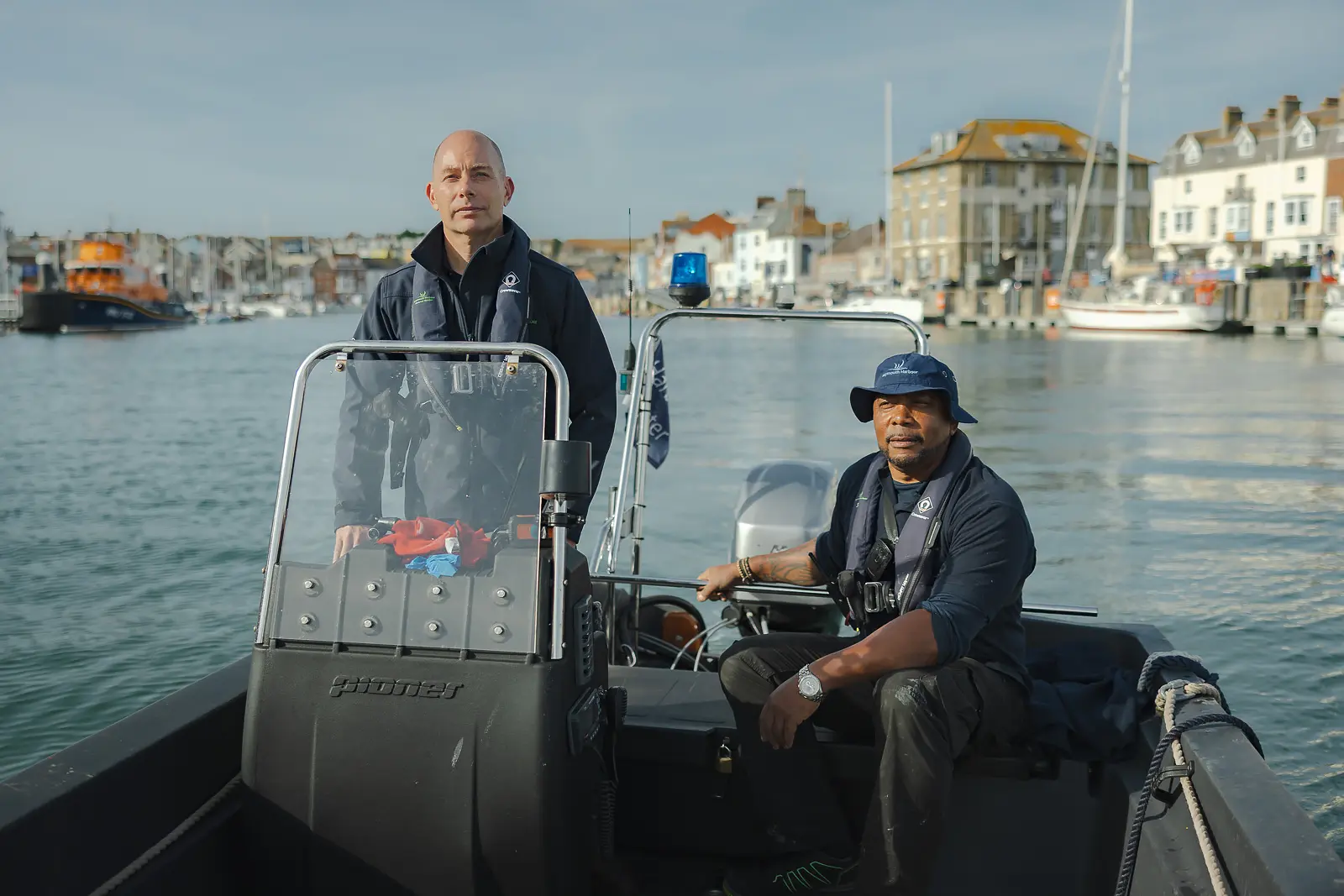Harbour Master and crew member seated in a patrol RIB on the water with Weymouth's colourful harbourside behind