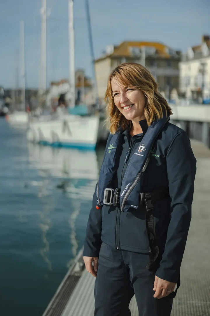 Harbour team member in life jacket standing on the quayside at Weymouth Harbour with sailboats and buildings behind