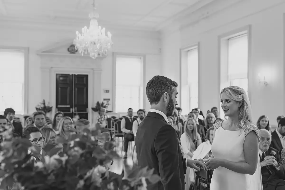 Bride and groom exchanging rings during their wedding ceremony at Poole Guildhall with guests watching.
