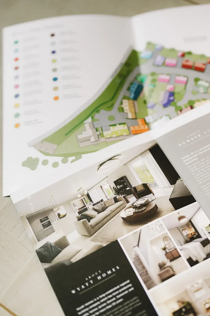 Open property development marketing brochures showing a colour-coded site plan and interior photography spread laid on a surface