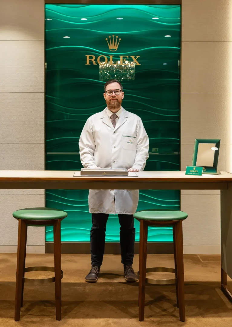 Rolex certified watchmaker in a white lab coat at a service counter inside a Rolex boutique in Dorset