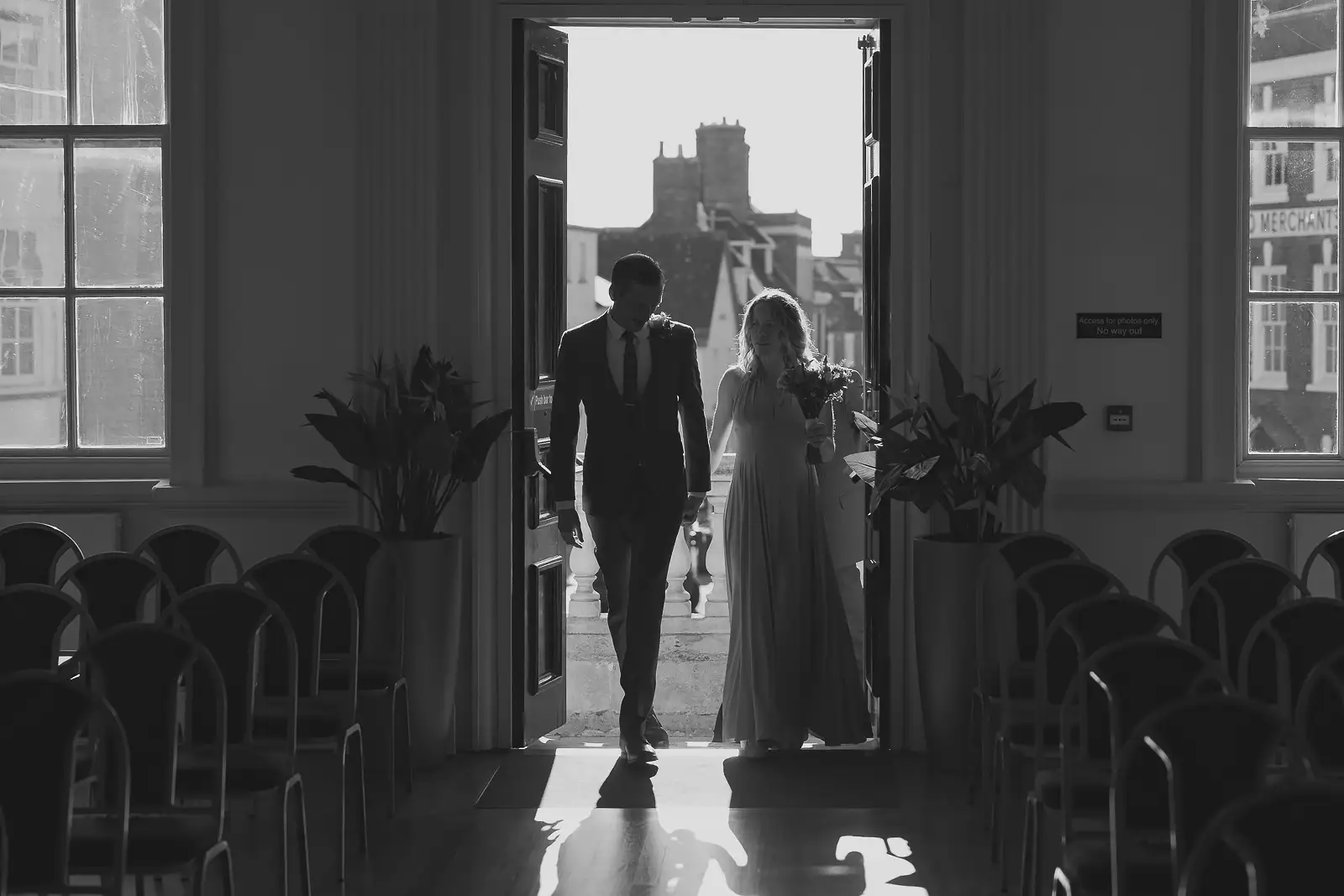 Striking black and white silhouette of couple entering Poole Guildhall ceremony room through open doorway, Poole town visible behind