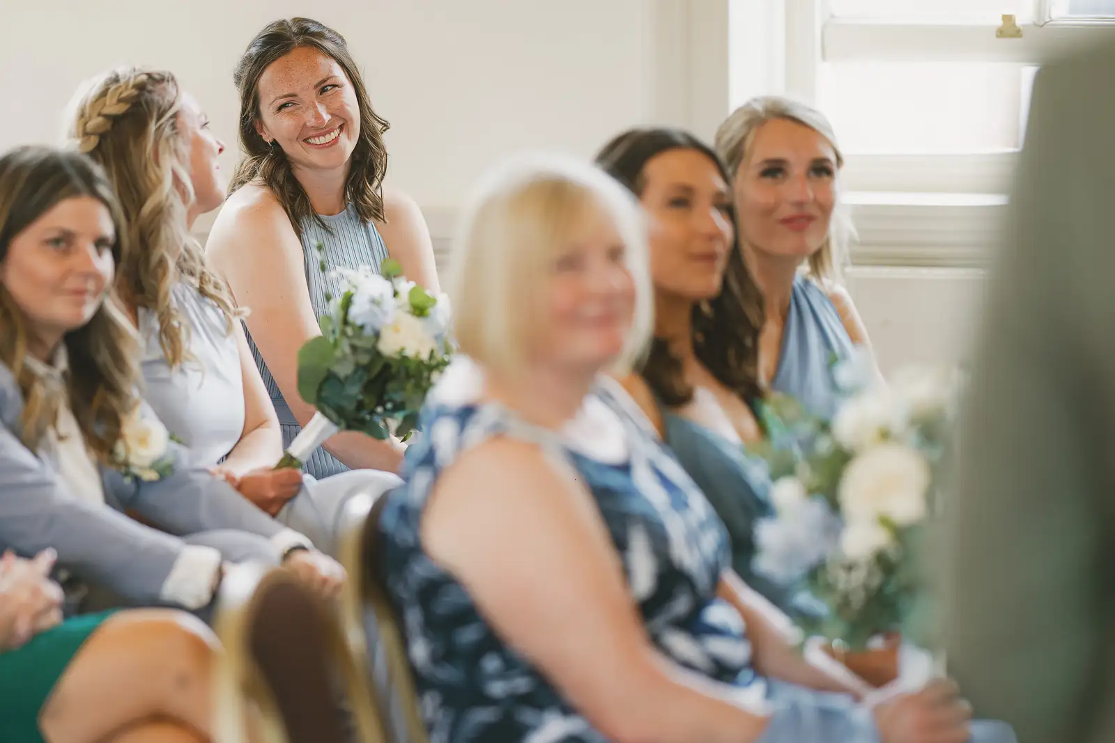 Smiling wedding guests and bridesmaids in blue seated watching the ceremony at Poole Guildhall Registry Office