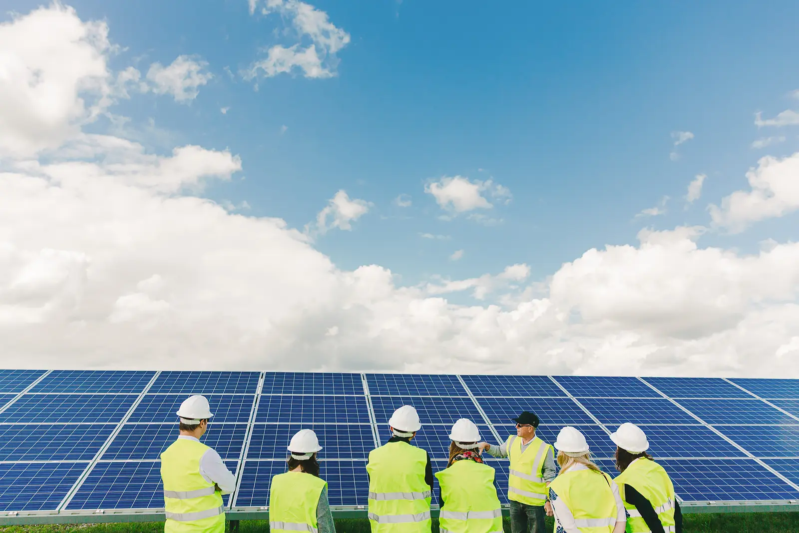 Team in high-visibility jackets and hard hats inspecting a solar panel array under a blue sky, Dorset PR photography
