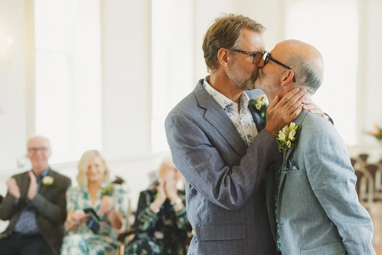 Two grooms sharing their first kiss as newlyweds at Poole Guildhall registry office, guests applauding behind them