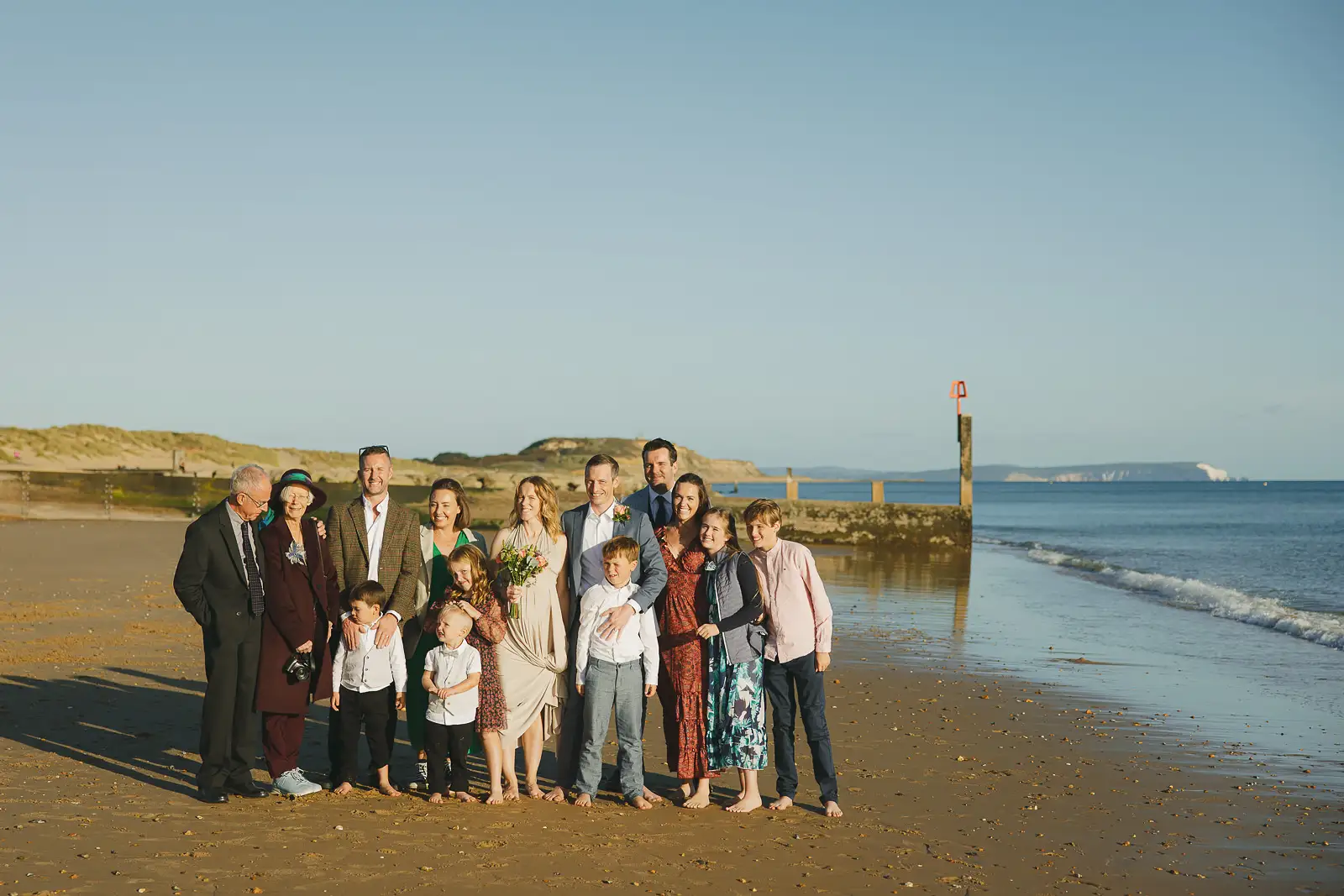 Wedding couple and family group on Bournemouth beach at golden hour, sand dunes and coastal headland behind