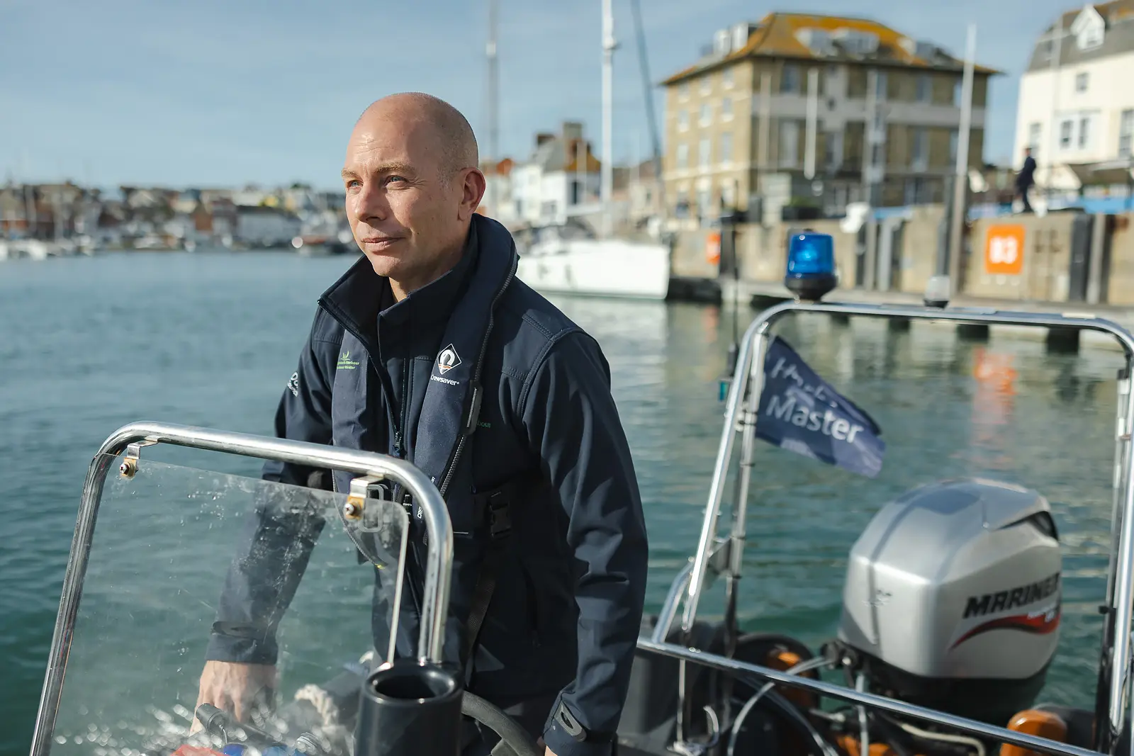 Harbour Master at the helm of a patrol boat on the water at Weymouth Harbour with the stone harbourside behind