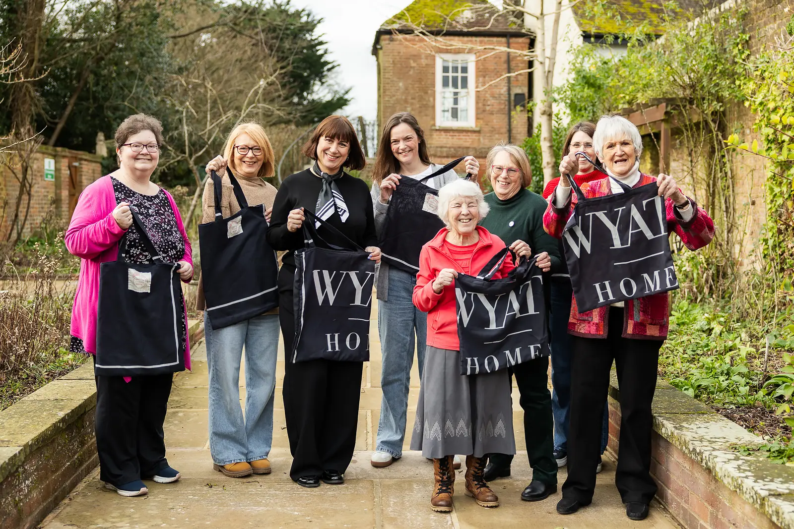 Group of women holding Wyat Home branded tote bags at an outdoor garden launch event in Dorset