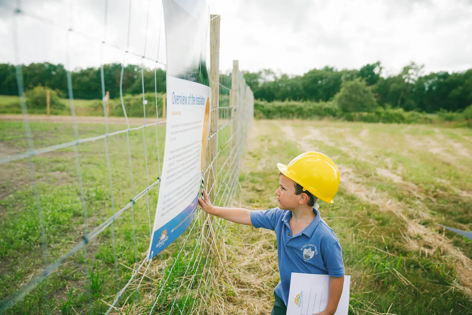 Young visitor in a yellow hard hat reading an information board at an outdoor solar farm site in Dorset