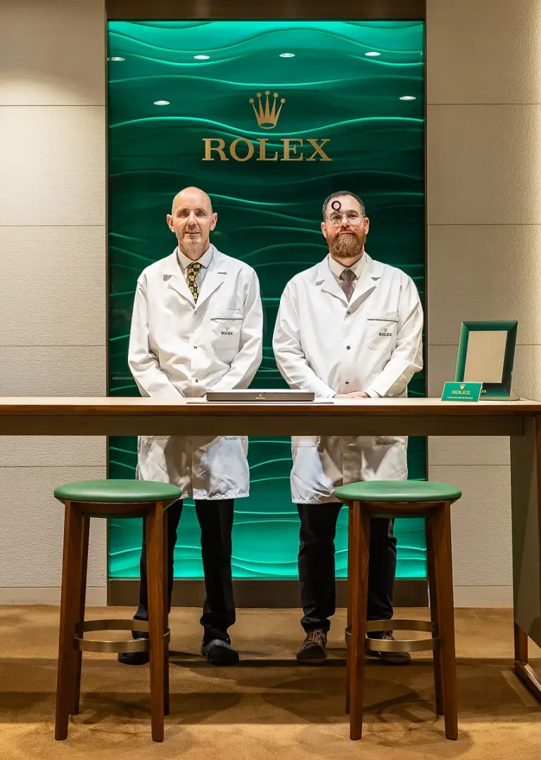 Two Rolex watchmakers photographed behind a service counter during a luxury brand photography shoot in Bournemouth.