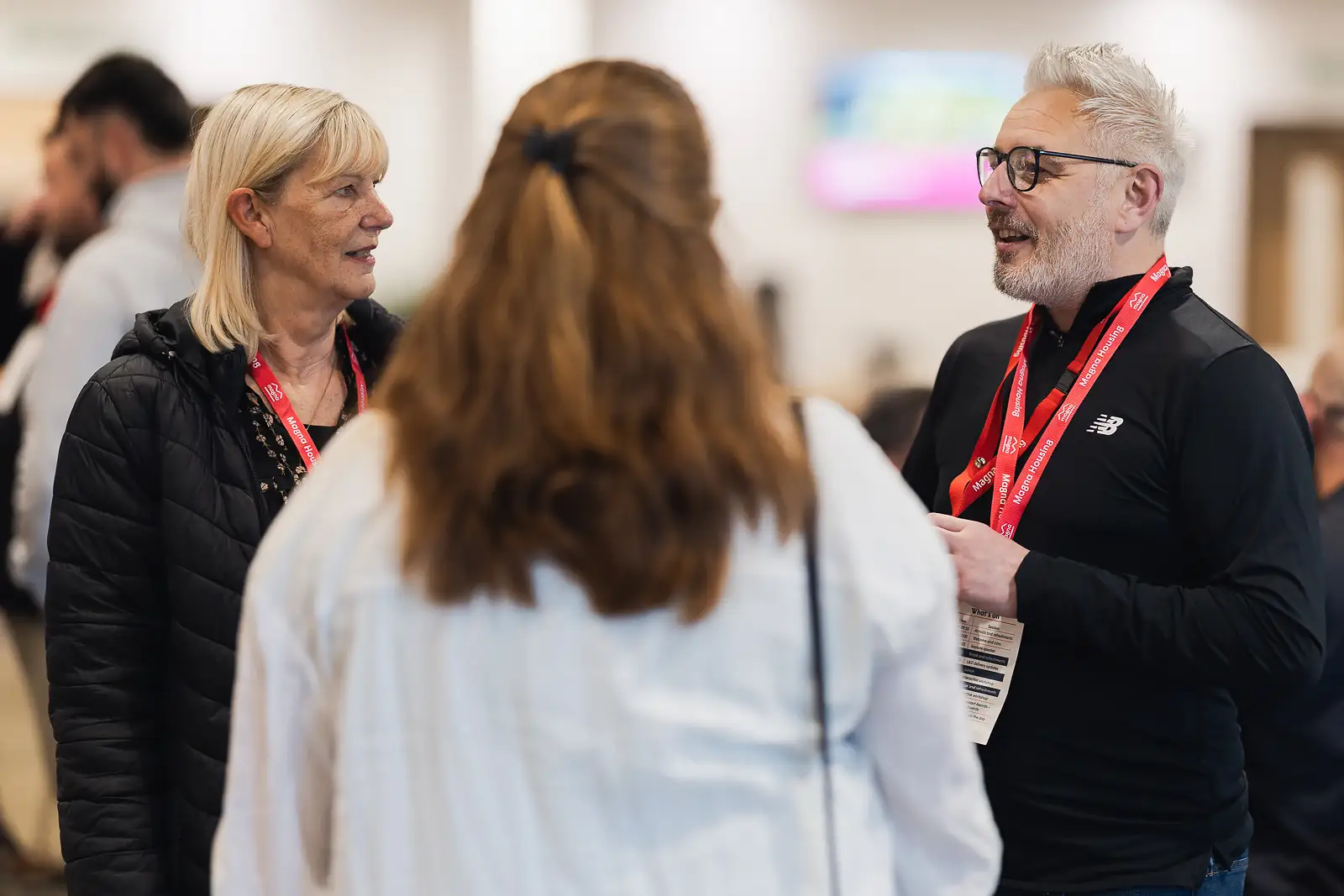Three colleagues in candid conversation wearing lanyards during a corporate away day event in Yeovil Somerset