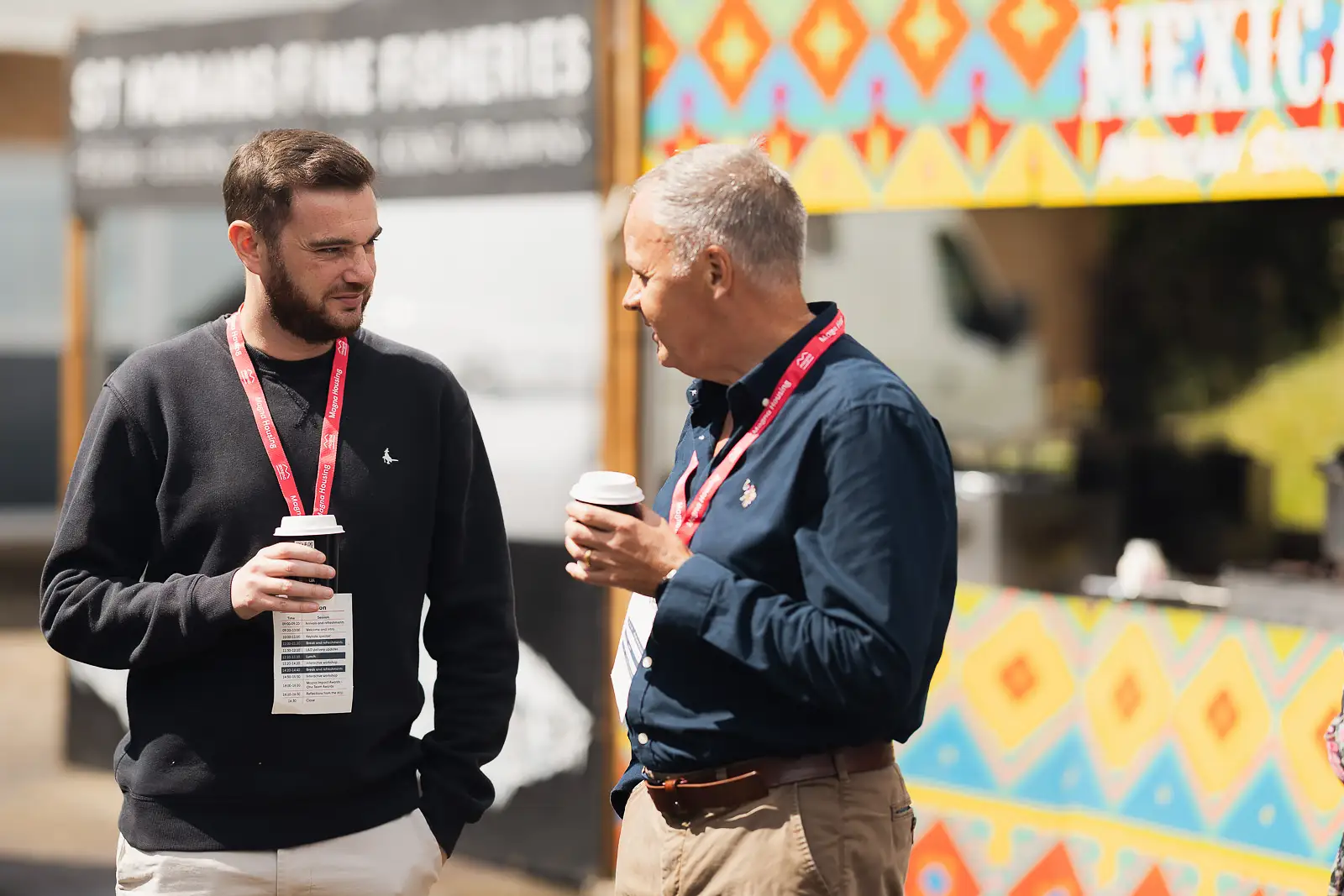 Two male colleagues holding coffee cups in conversation during an outdoor break at a corporate away day at Westlands Theatre