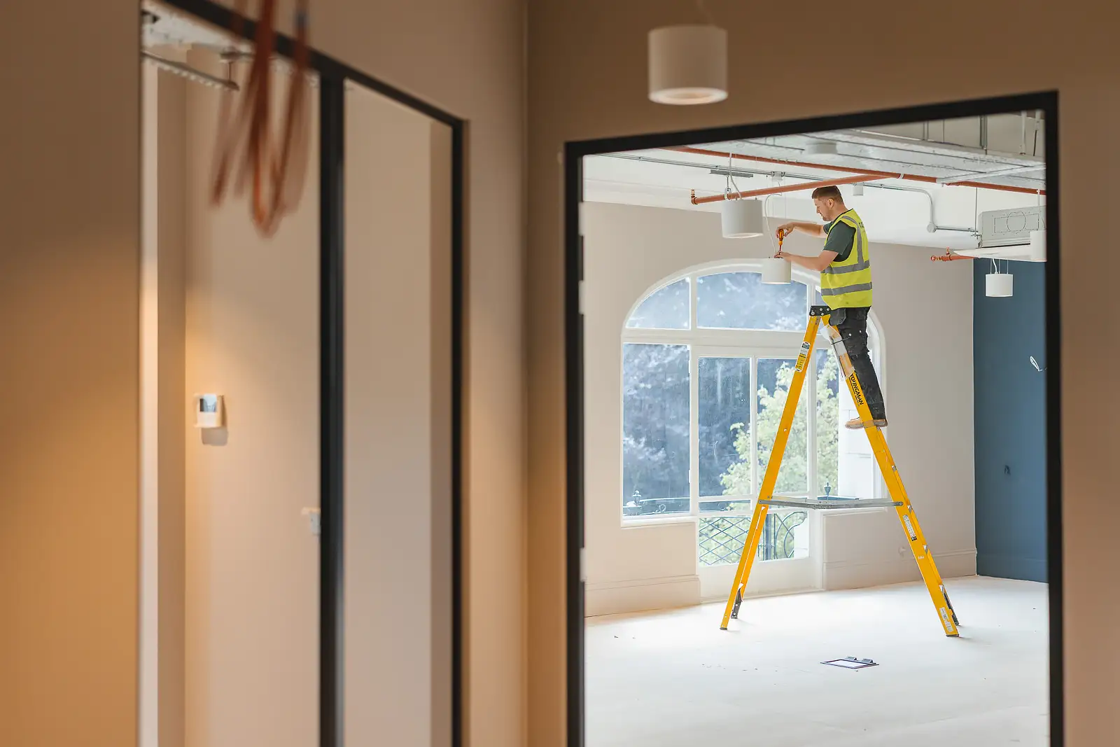 Hero shot: worker framed through two glass partition doorways, original Bobby's arched window beyond — Bournemouth commercial photography