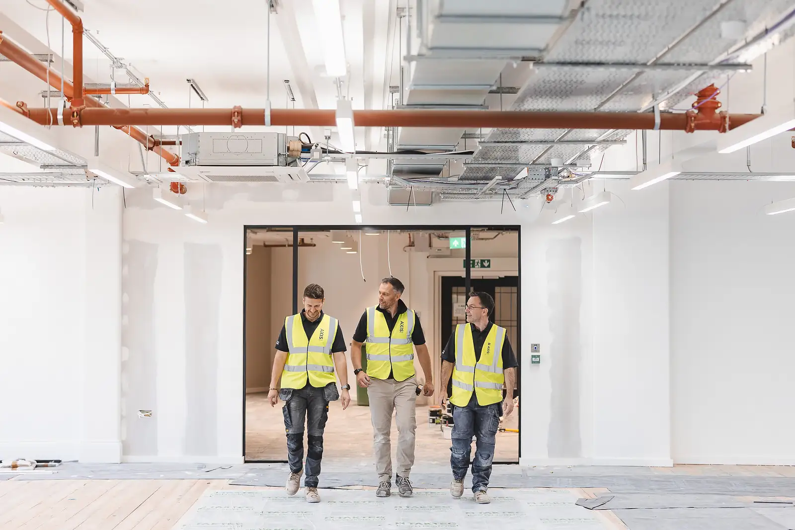 Three-man team photographed walking through glass partition doors, copper pipe services above — commercial photography in Bournemouth