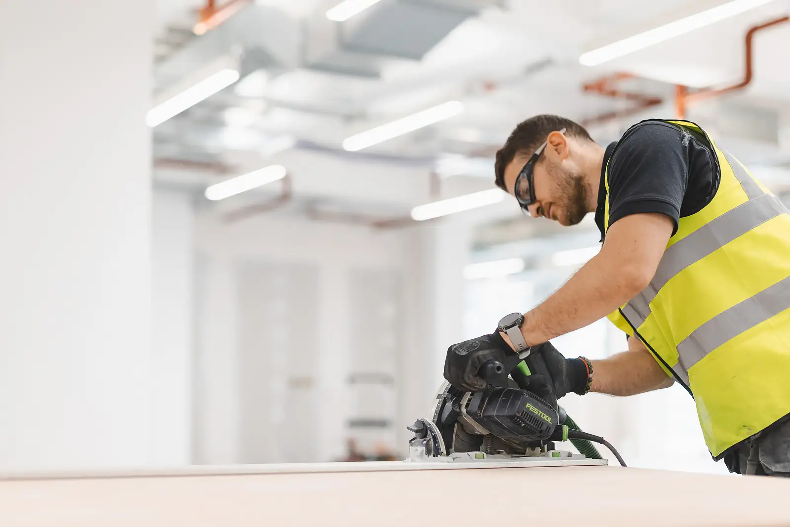 Close portrait of a joiner operating a Festool circular saw, safety glasses and gloves — editorial commercial photography on site