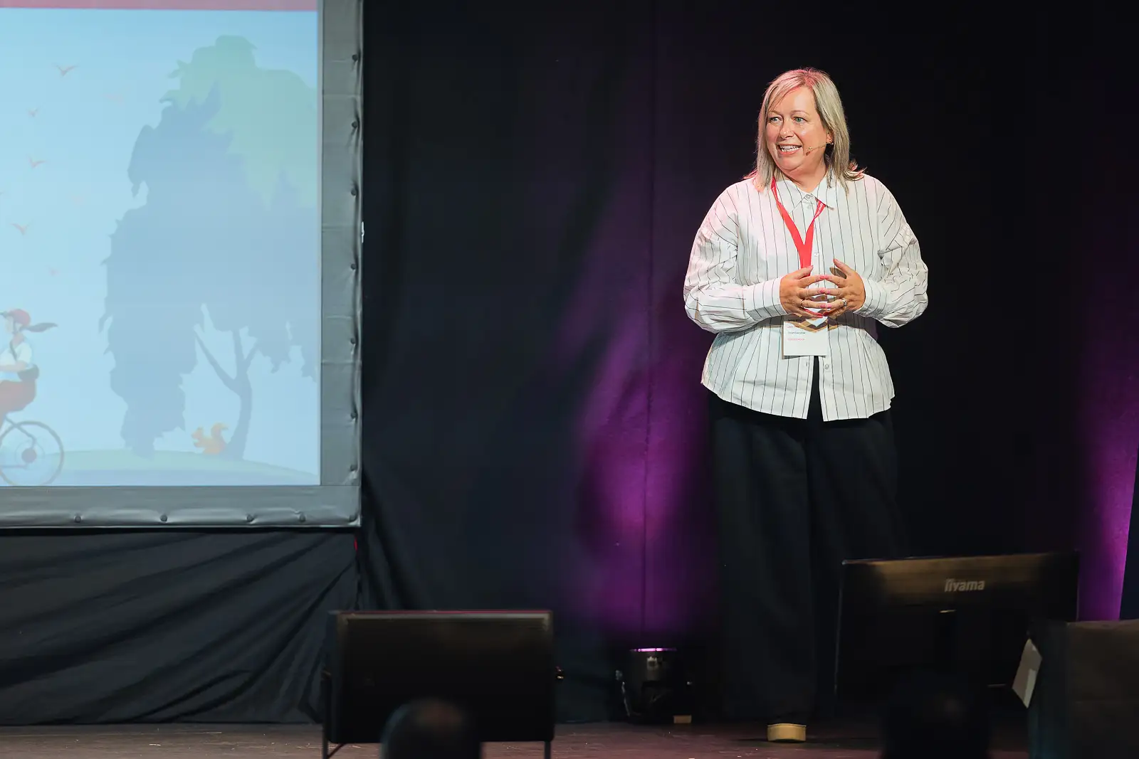 Female speaker presenting on stage with a projected slide behind her at a corporate conference in Somerset, documentary conference photography