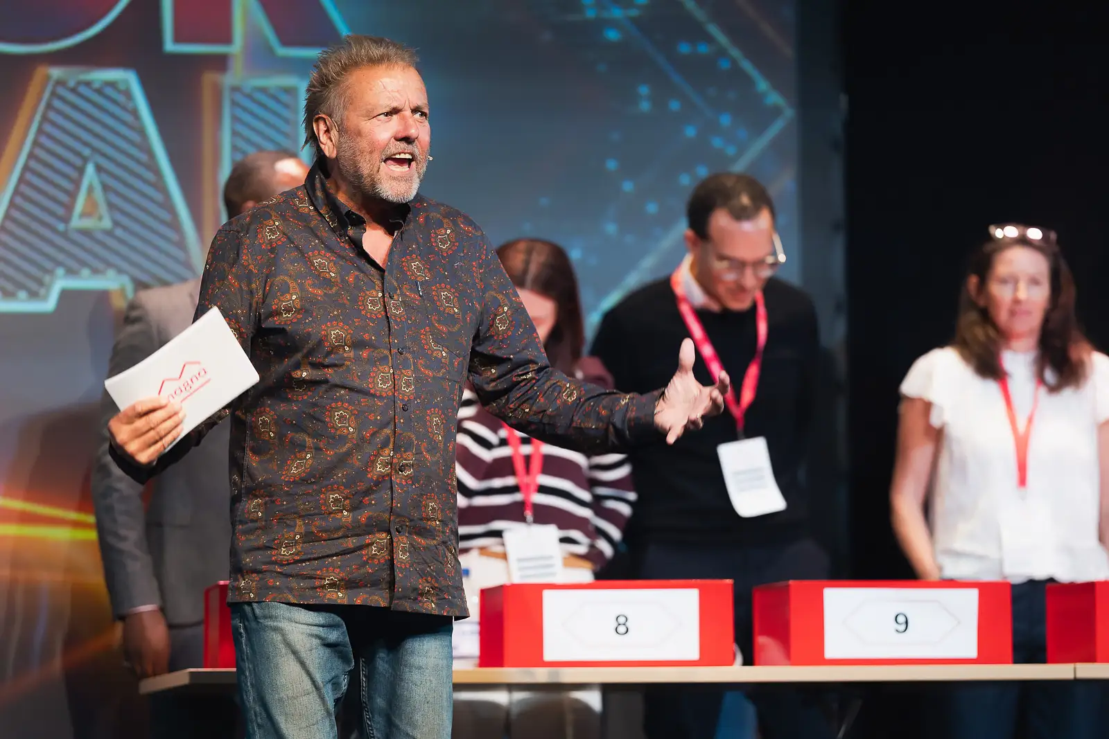 Event host gesturing energetically on stage during a team participation activity at a corporate away day