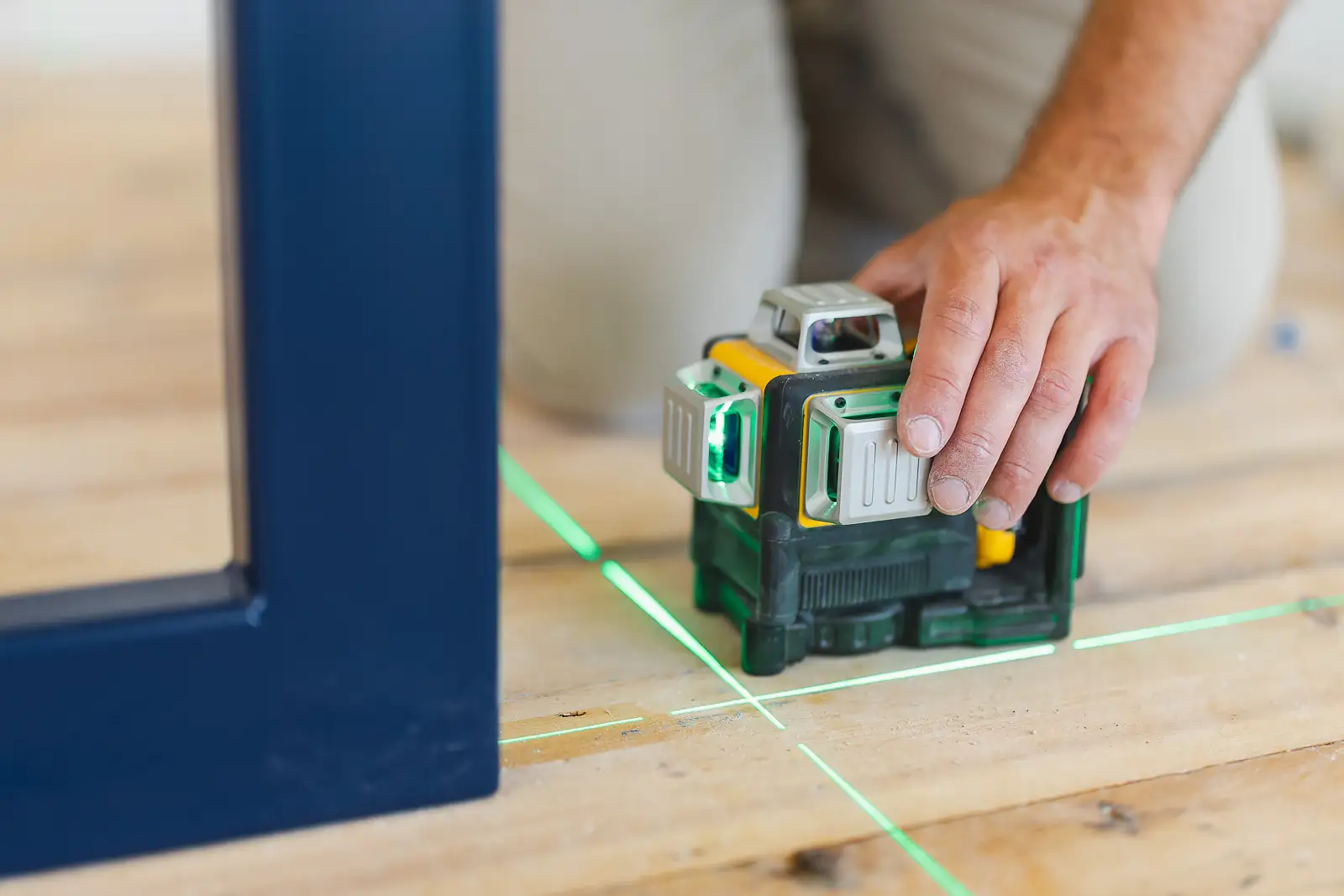 Close-up detail of a hand resting on a laser level, green level lines projected across the site floor