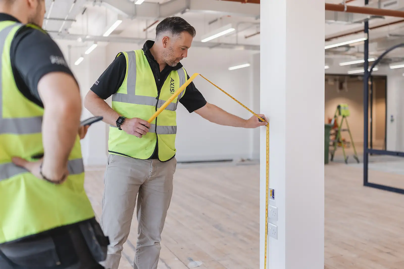 Senior site manager using a tape measure to check the dimensions of a structural column during a quality inspection