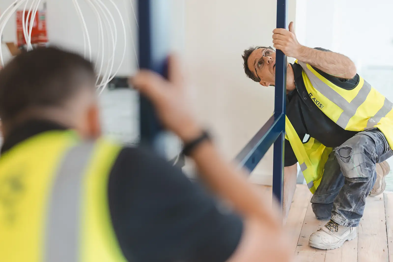 Close-up of a worker checking steel frame alignment with a screwdriver, safety glasses on, shallow depth of field