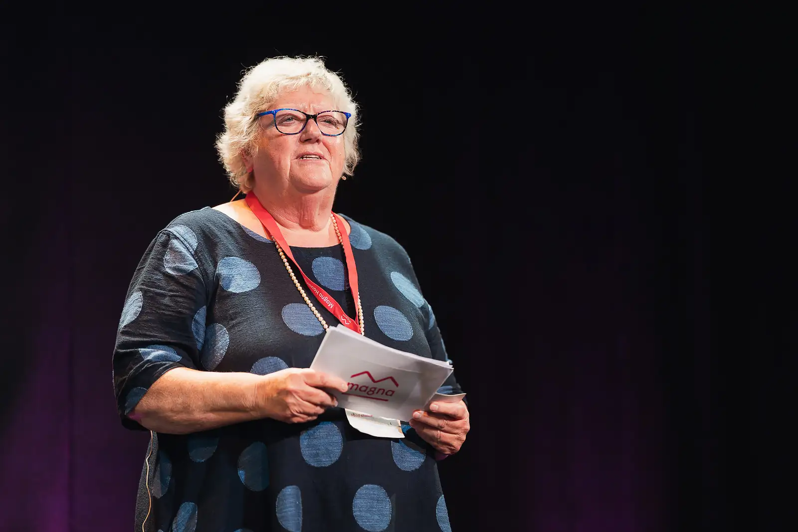 Senior leader addressing colleagues from the stage holding notes during a corporate event, captured with documentary event photography