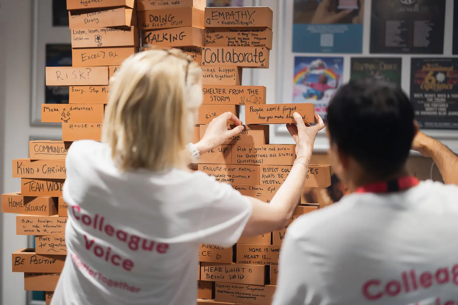 Colleagues stacking cardboard bricks inscribed with company values during a team-building activity at a corporate away day event