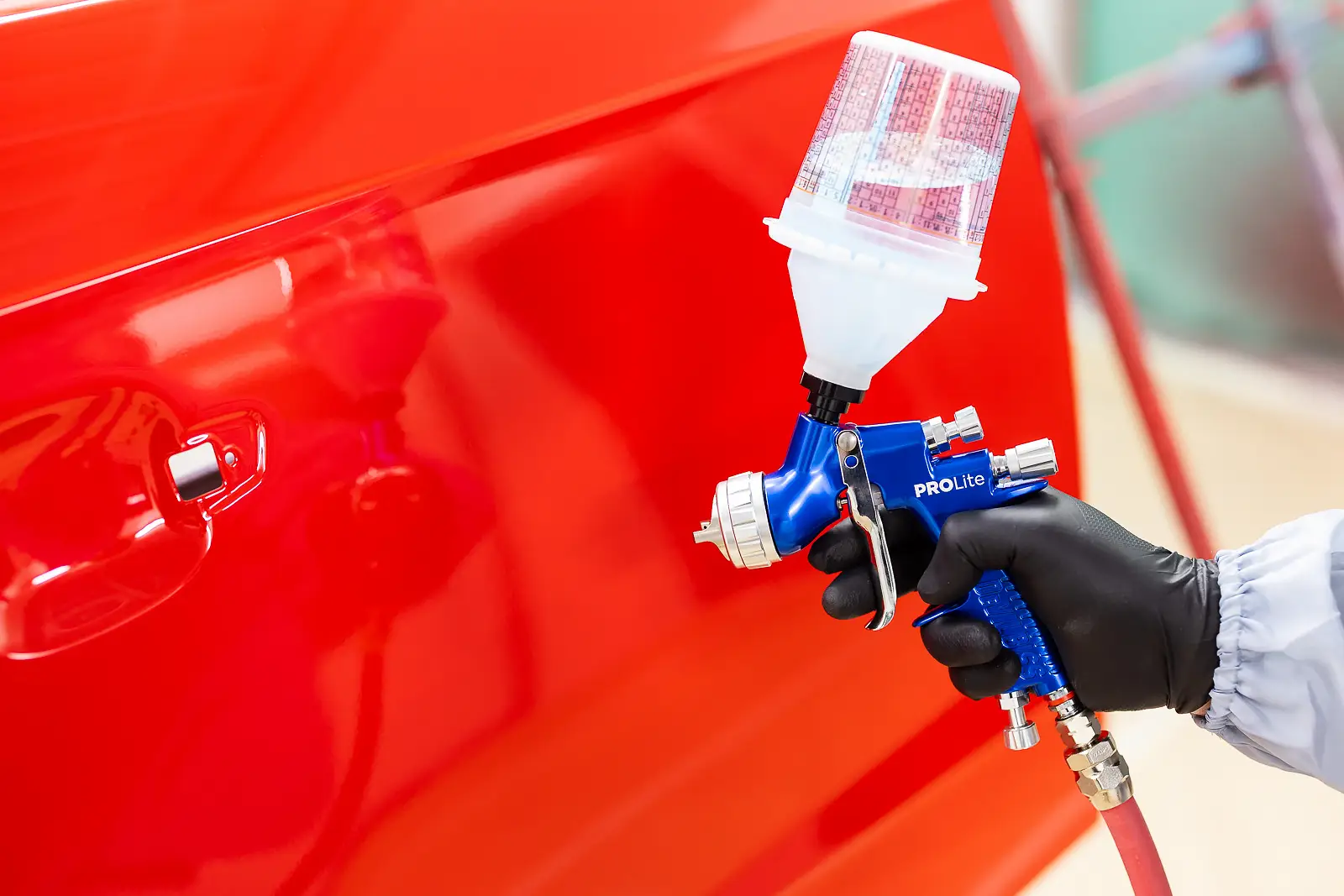 Gloved hand holding a spray gun to a red car door during a respray, shot for a Bournemouth advertising campaign