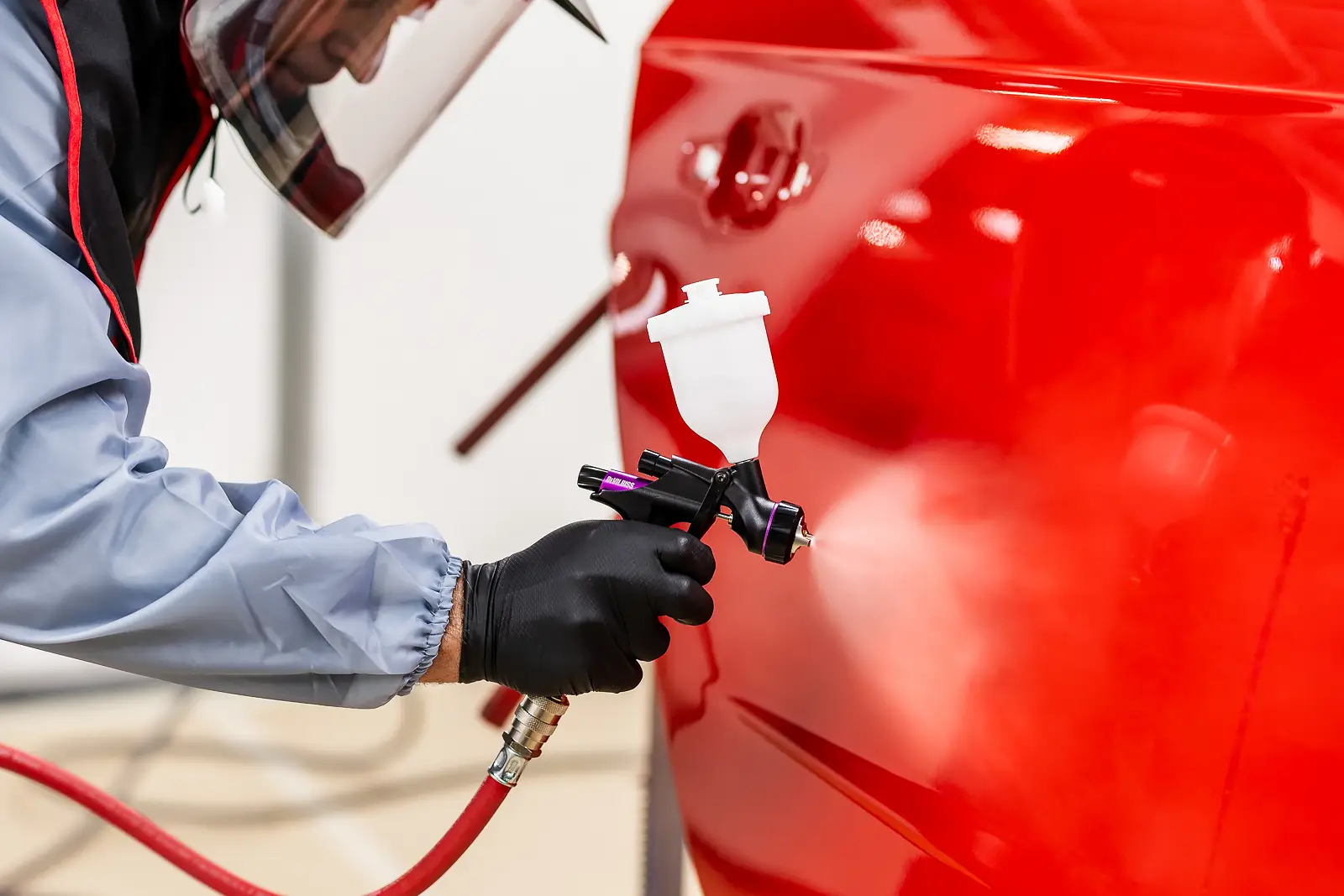 Technician spraying a red car panel in a workshop, part of a Dorset campaign photography shoot