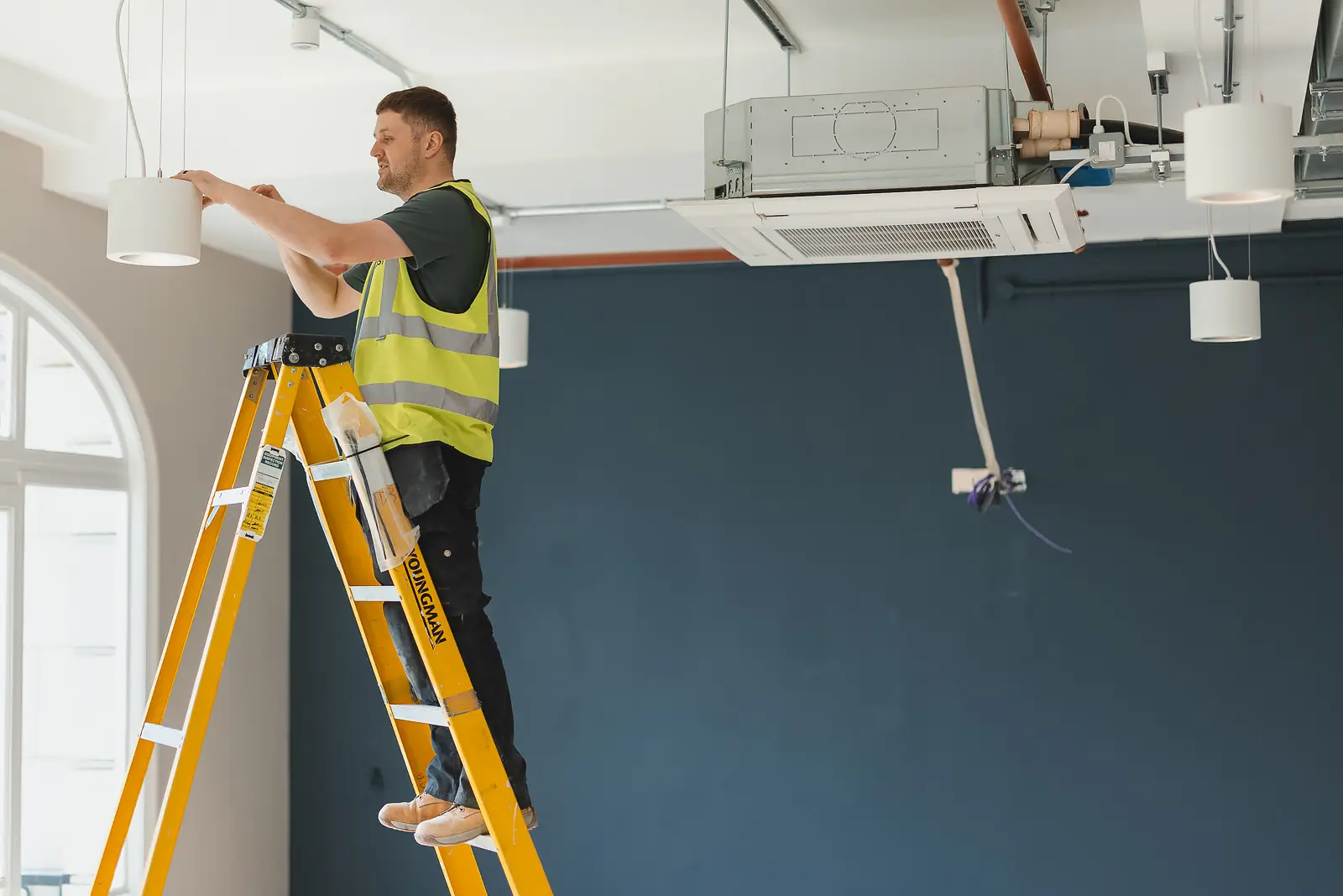 Tradesman on a ladder installing a pendant light, from a Bournemouth commercial photography shoot