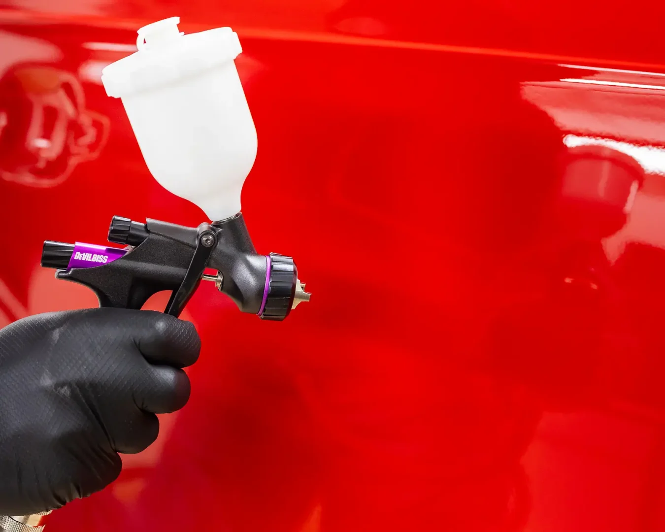 Spray gun held close to a glossy red car panel, captured for a Bournemouth product photography campaign