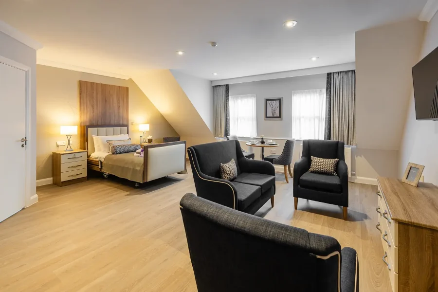 Spacious bedroom with an adjustable bed, bedside furniture and a separate seating area with dark armchairs.