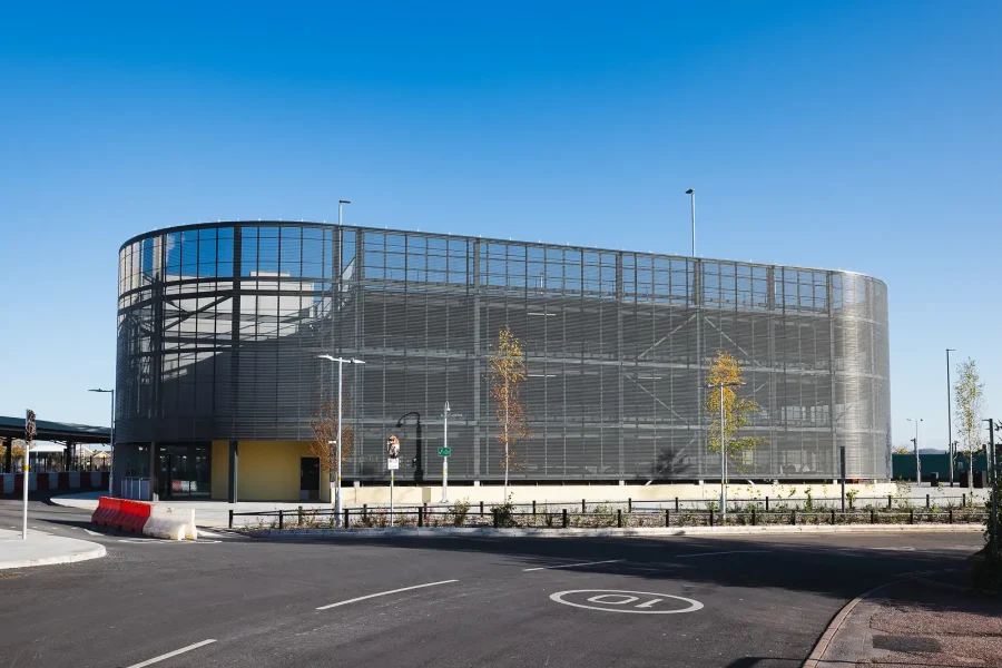 Curved multi-storey car park facade with visible steelwork and an access road in the foreground.