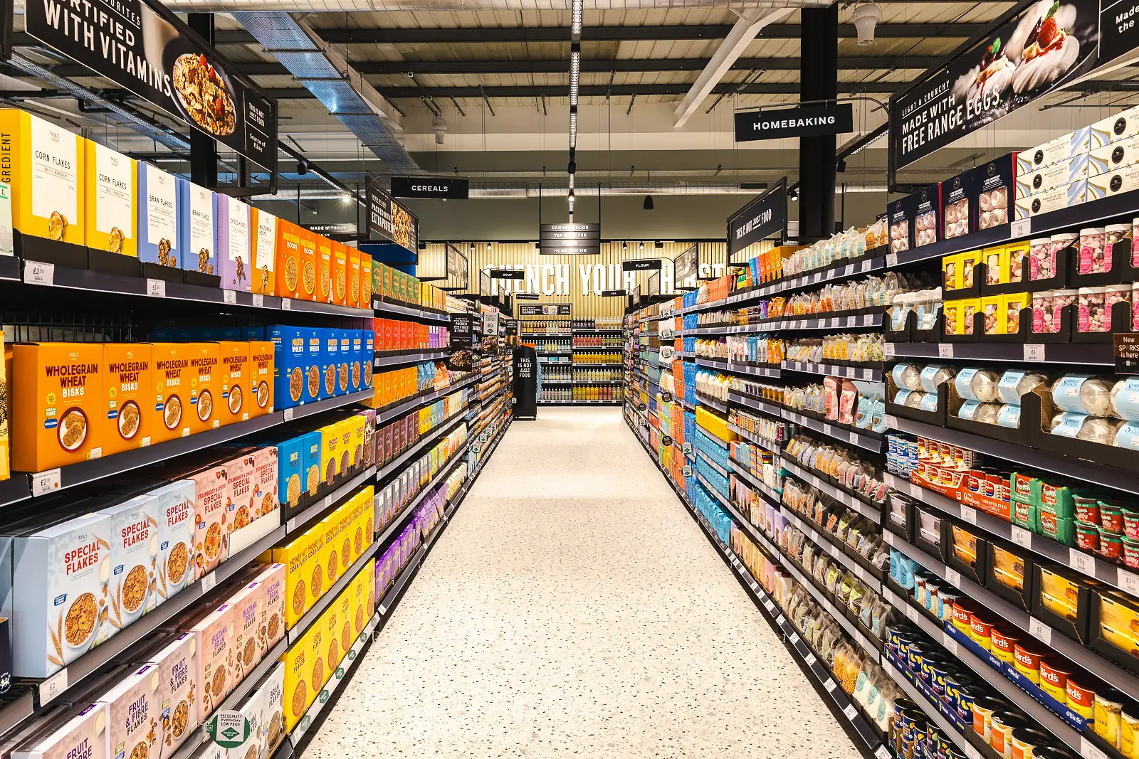 Stocked cereal shelves and overhead signs viewed along an aisle before the Poole store opening.
