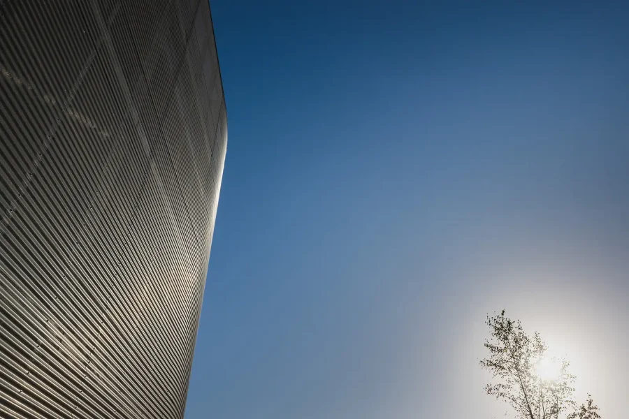 Close exterior view of a curved metal-clad facade against a clear blue sky.