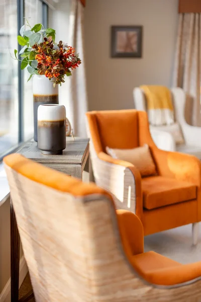 Orange armchairs beside a lounge window, with flowers on the windowsill.
