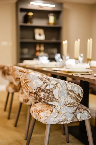 Patterned upholstered dining chairs beside a table set with glasses and candles.