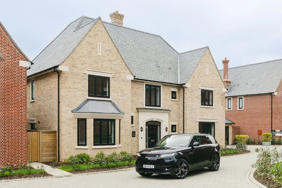 Stone-fronted detached house with a slate roof, landscaped front garden and a car on the driveway.
