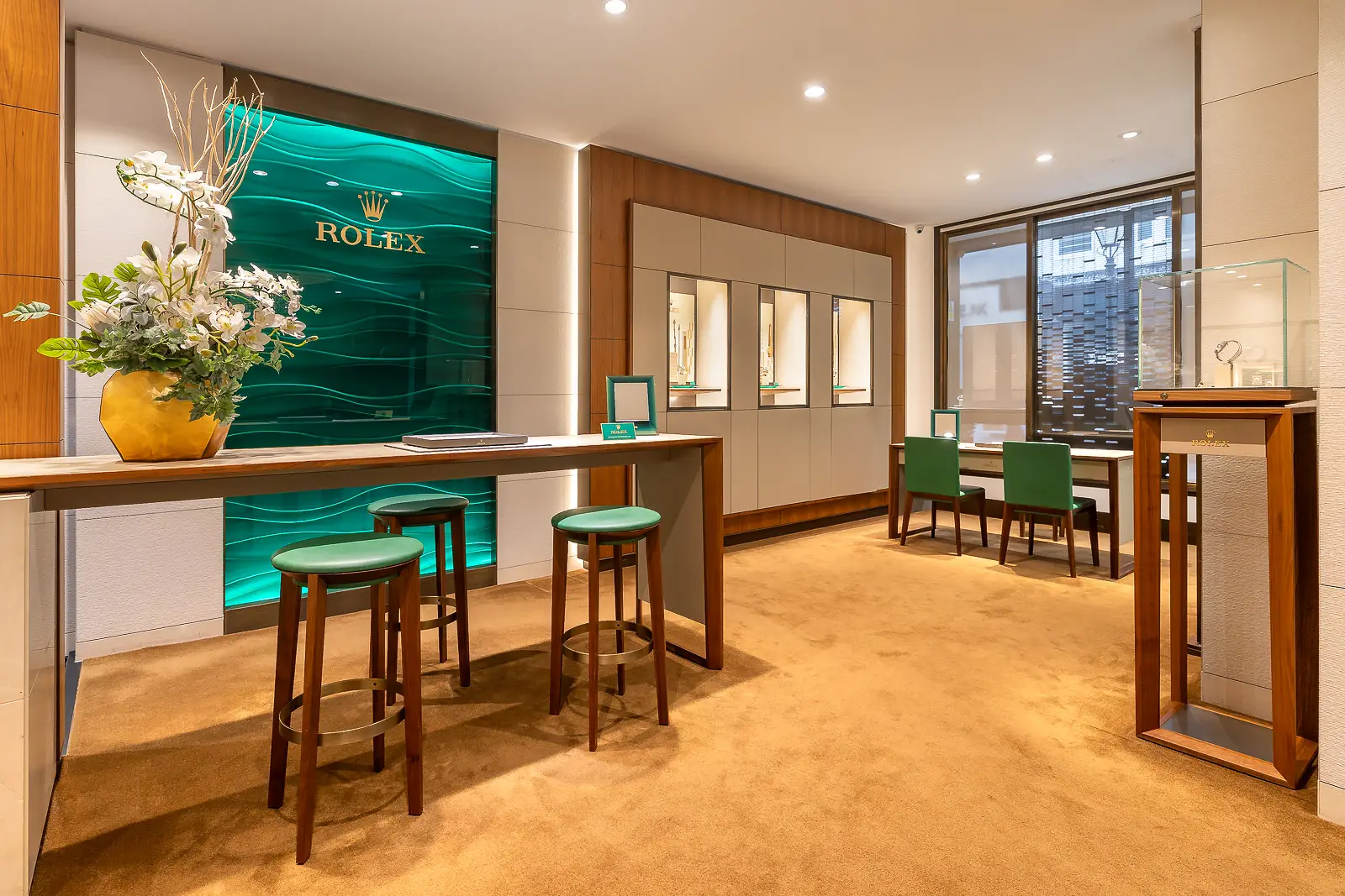 Watch showroom with glass display cabinets, a consultation counter, green seating and wood finishes.