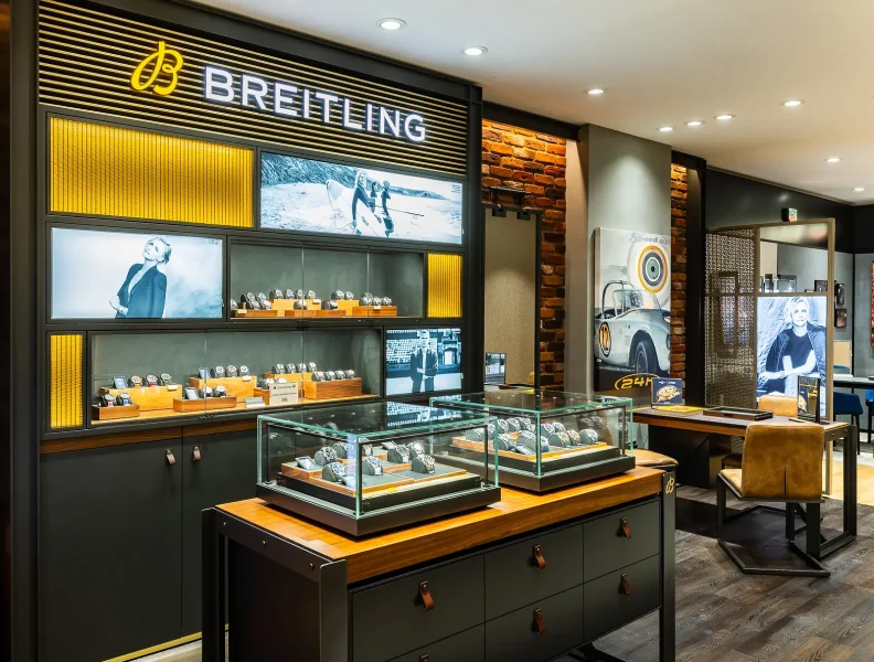 Watch shop interior with illuminated wall displays, glass counters and dark fittings.